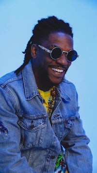 a man with dreadlocks wearing sunglasses and a denim jacket